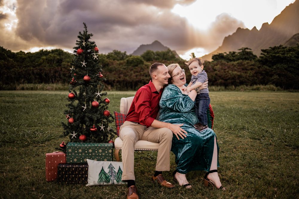 A joyful family portrait next to a Christmas tree with mountains and sunset clouds.