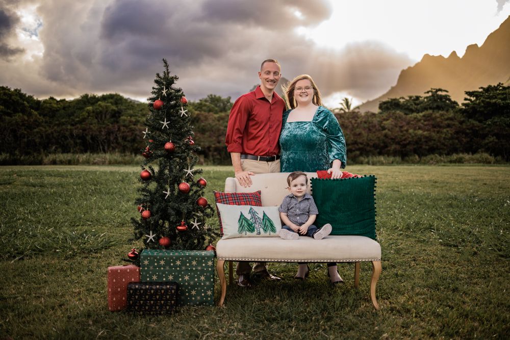 A decorated Christmas tree and wrapped presents displayed outdoors at sunset against a dramatic cloudy sky.