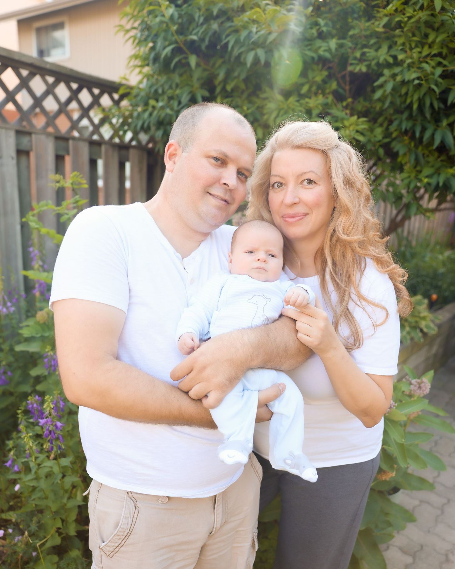 Family in white shirts poses together in a backyard garden setting.