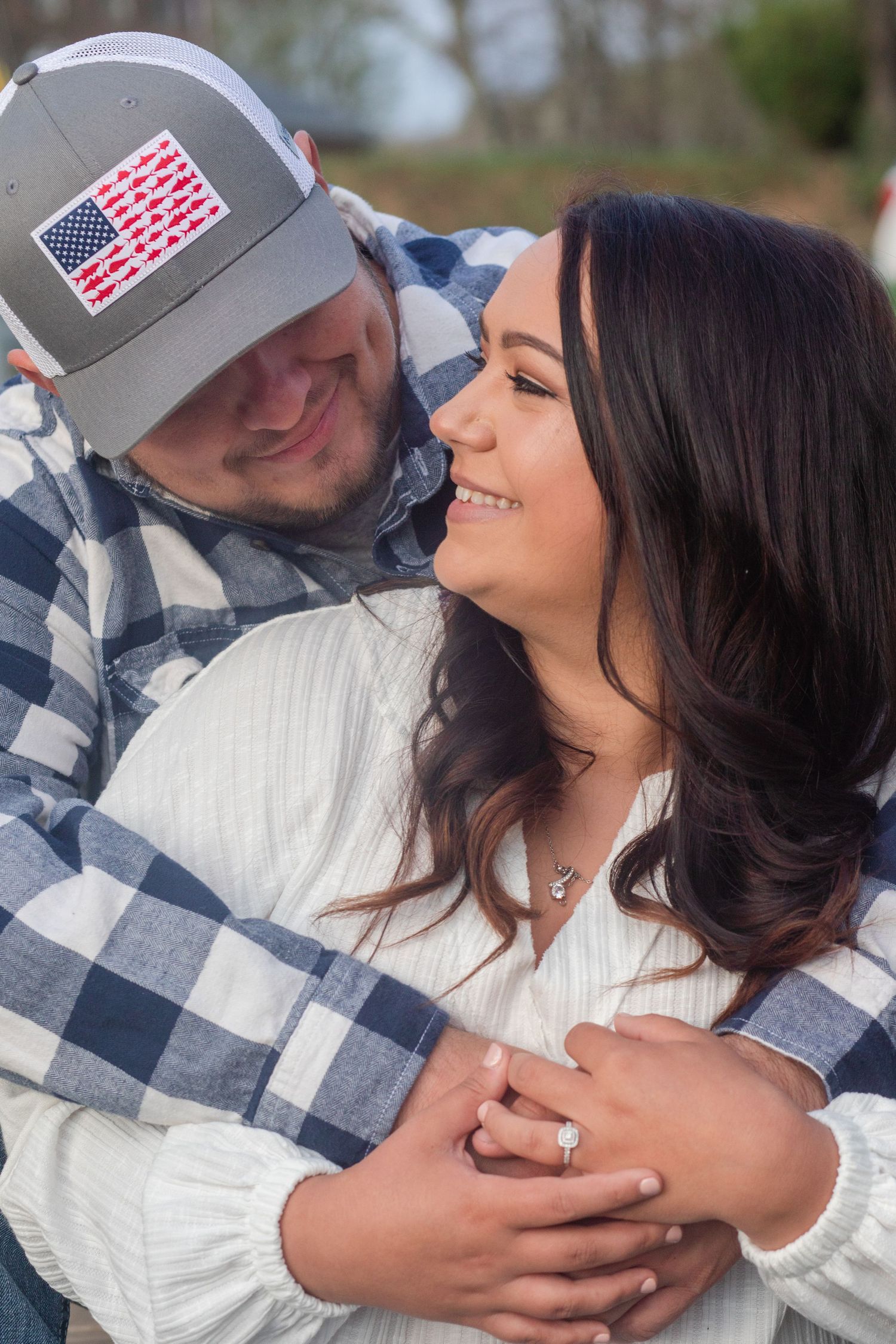 Close up of couple in plaid and white, sharing intimate moment with engagement ring visible.