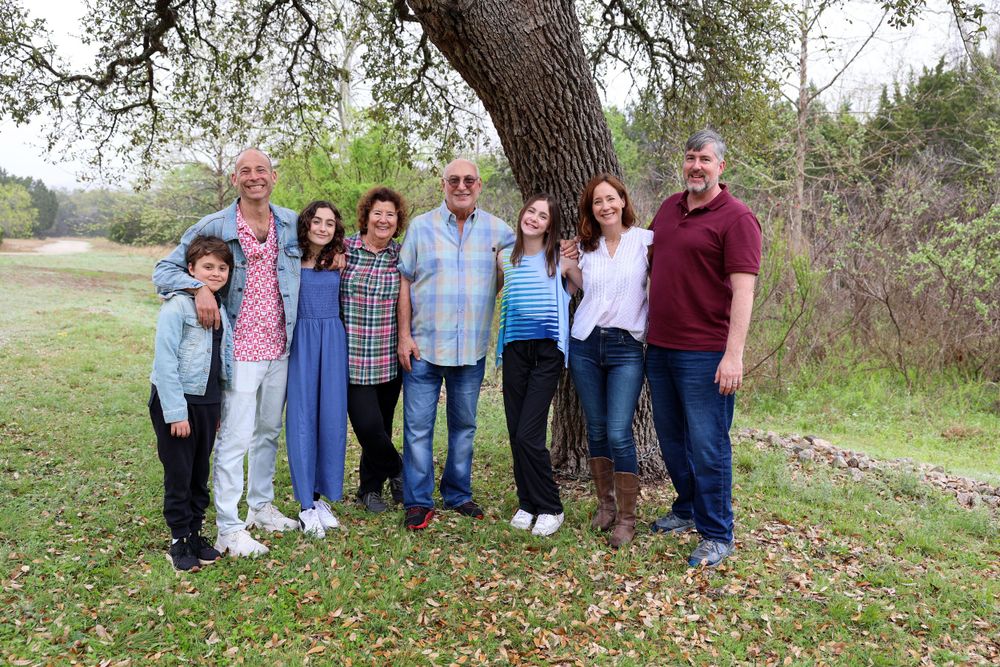 Multi-generational family posing together outdoors under a large tree on a sunny autumn day.