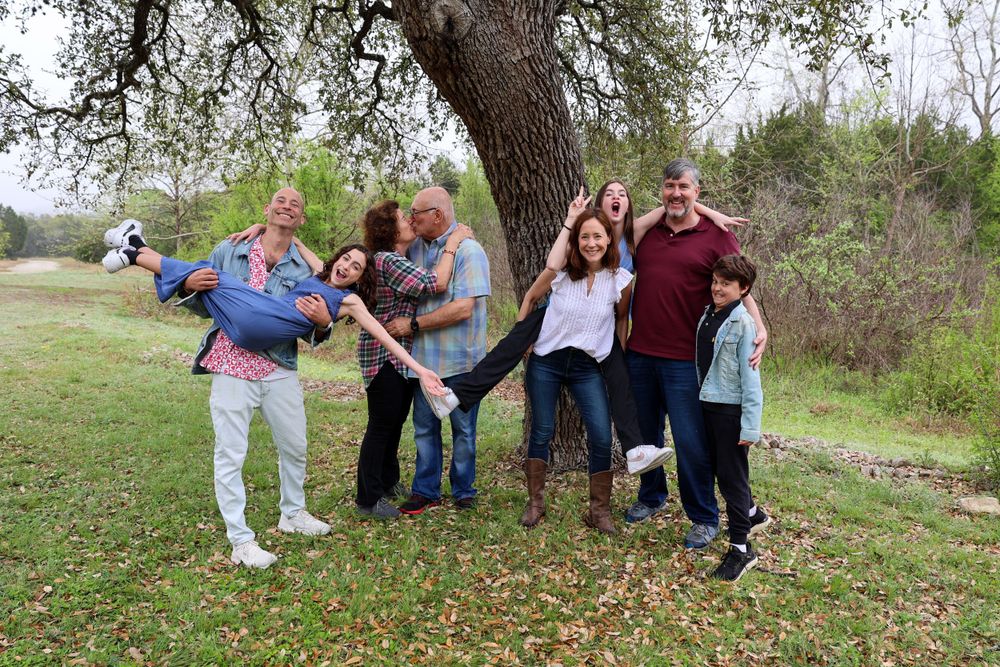 A fun family photo session with silly poses under a large tree in a natural setting.