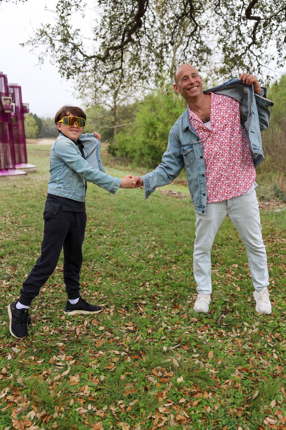 Two people in denim jackets hold hands while dancing and playing outdoors.