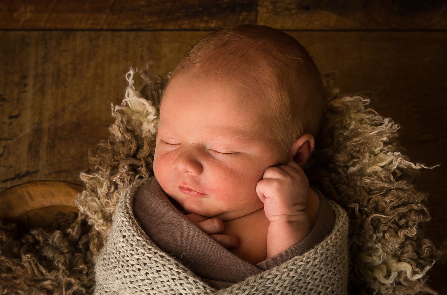 Sleeping newborn baby wrapped in knit blanket on textured backdrop.