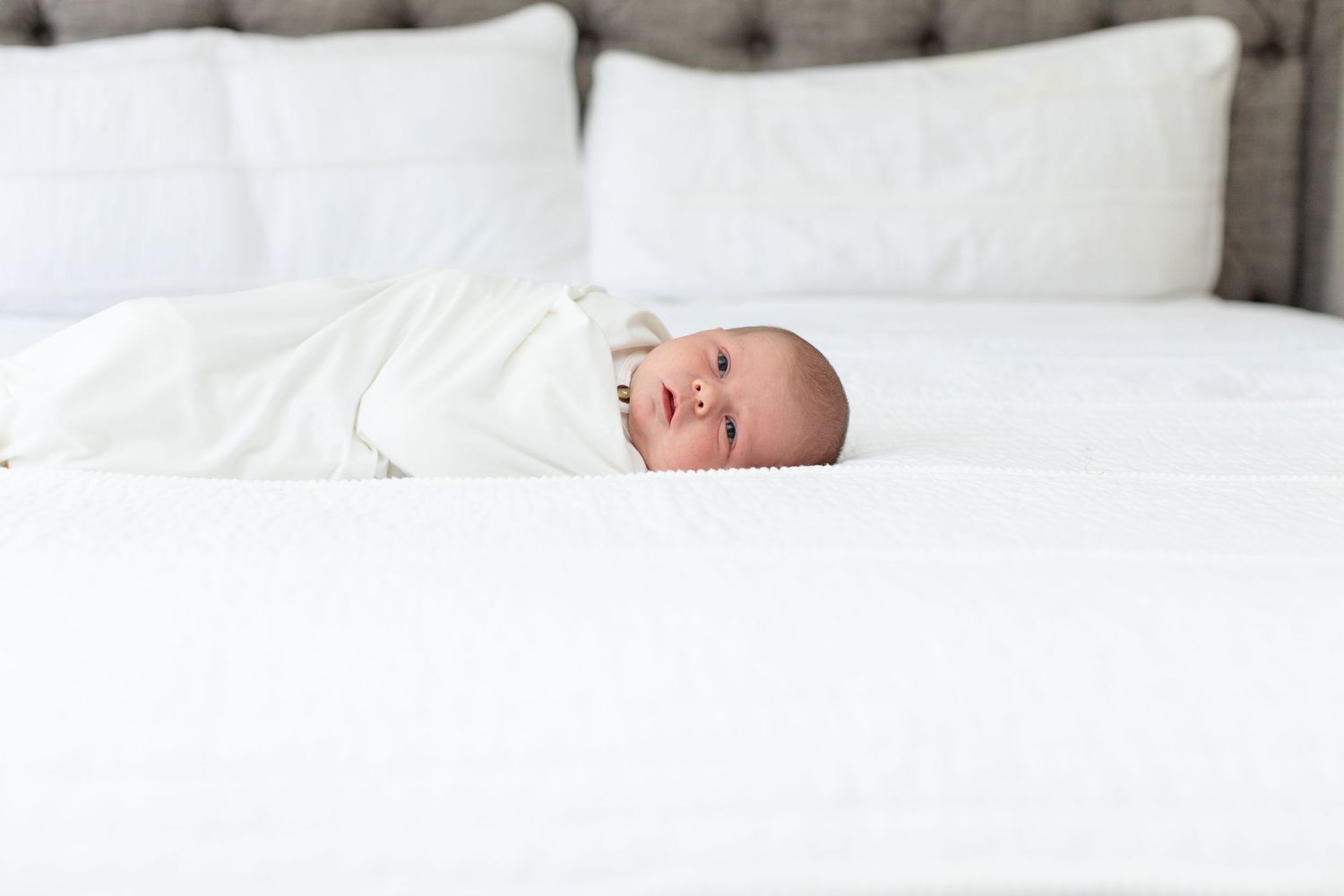 Newborn baby wrapped in white blanket lying on white bed.