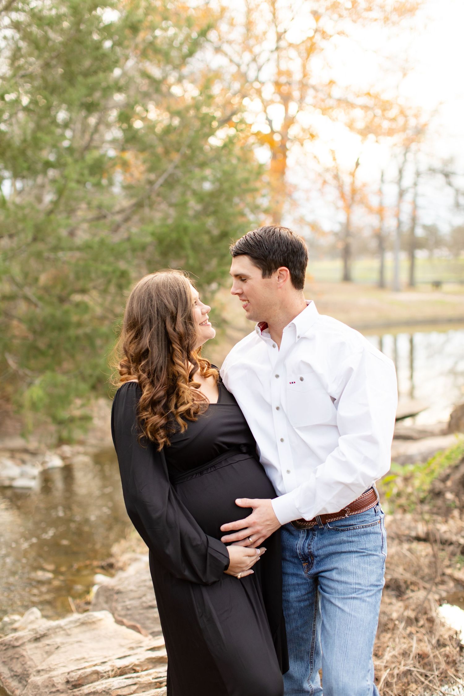 Side view of couple's maternity photo by water with matching black and white outfits.