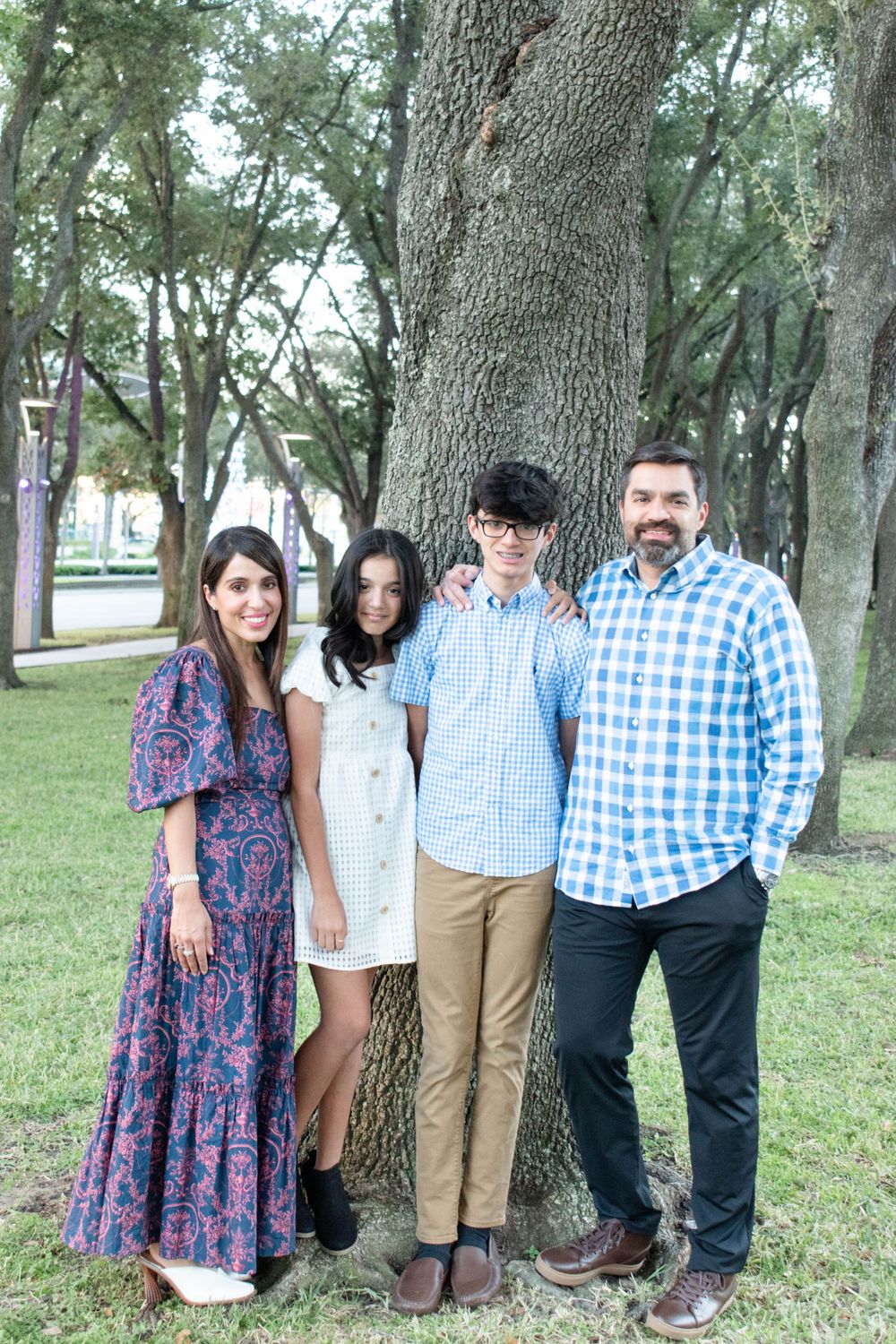 A family group poses by a large tree trunk in a park wearing coordinated casual outfits.