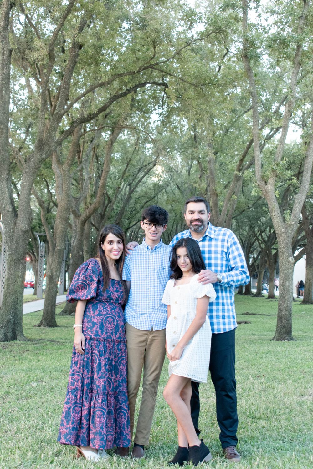 Family group portrait under green trees wearing coordinated blue and white outfits.