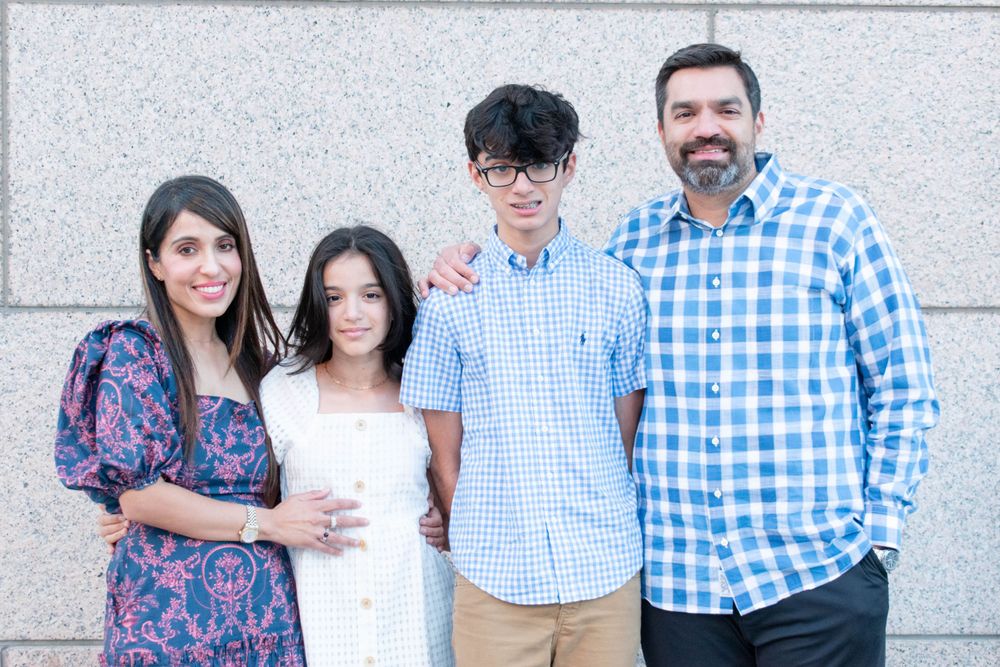 Family photo of four people wearing coordinating blue outfits standing against a light colored wall.