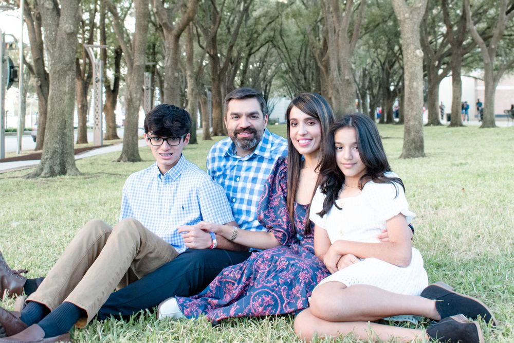 A family relaxes together on grass in a park with tall trees in the background.