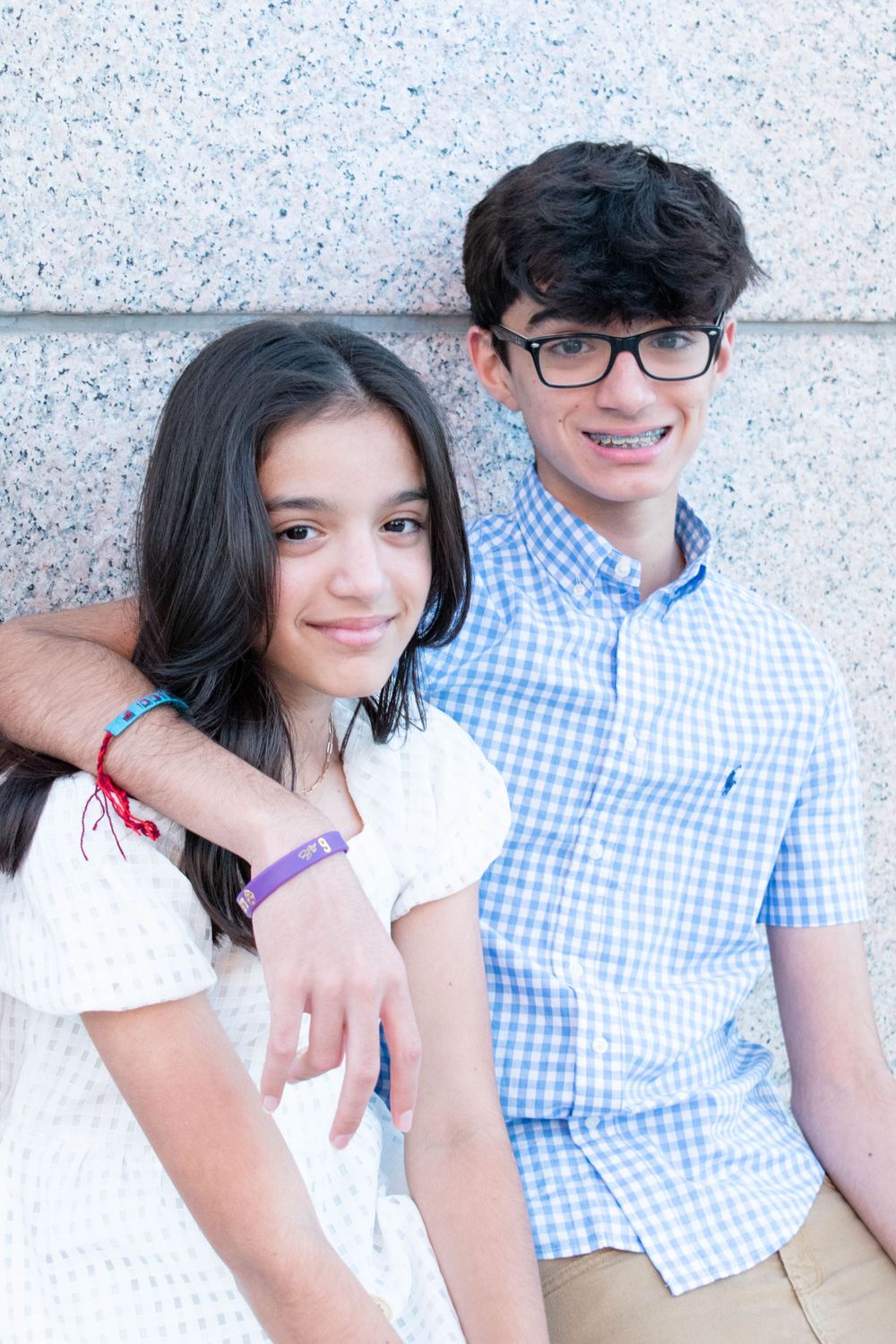 Two young people in coordinated blue and white outfits pose casually against a light wall.