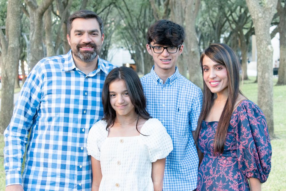 A family group stands together smiling in a park setting wearing coordinating blue and white outfits.