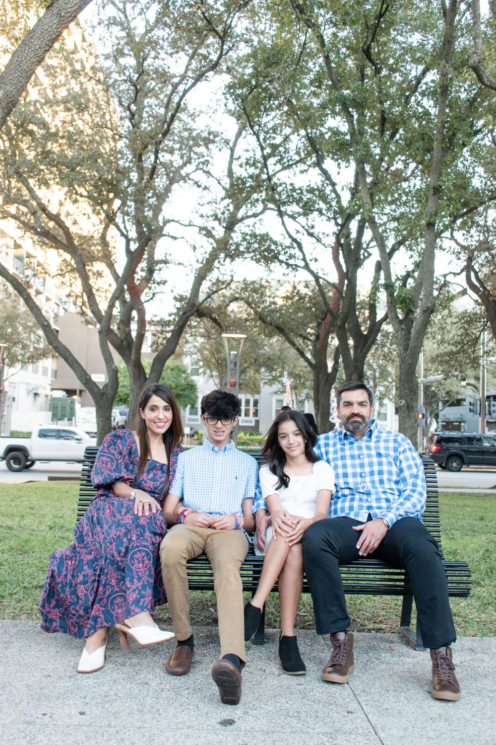 A family sits together on a park bench surrounded by leafy trees.