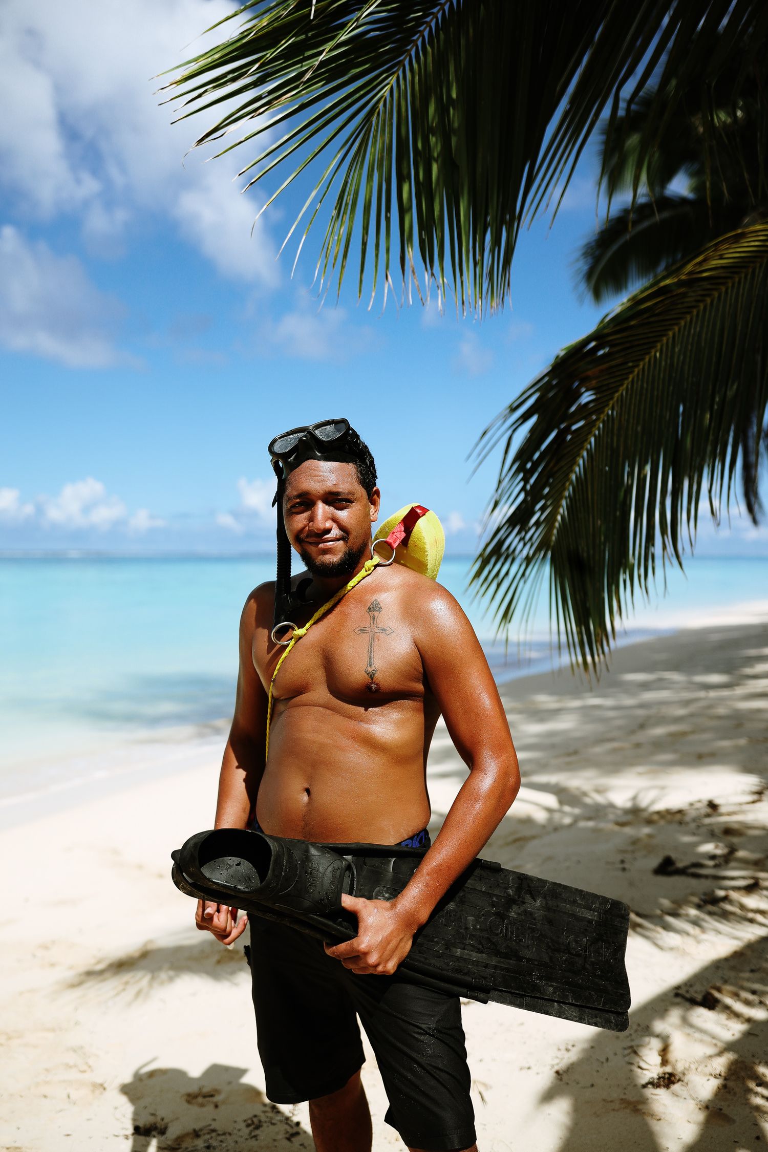 Beachgoer with snorkel equipment poses under palm fronds on tropical shoreline.
