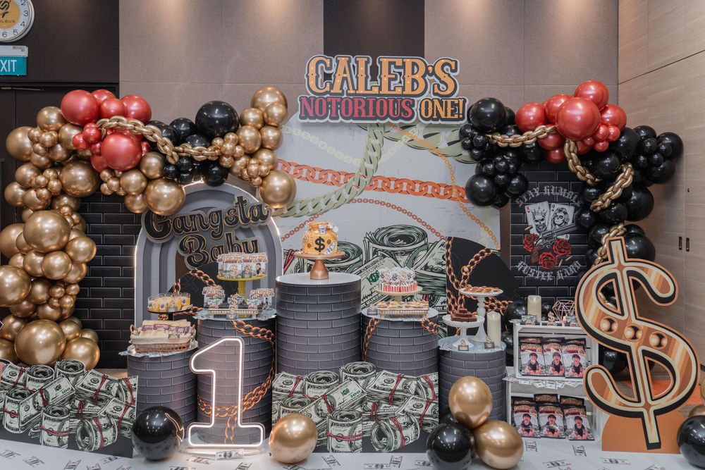 Money themed party display with gold and red balloon decorations, dollar signs, and dessert stands.