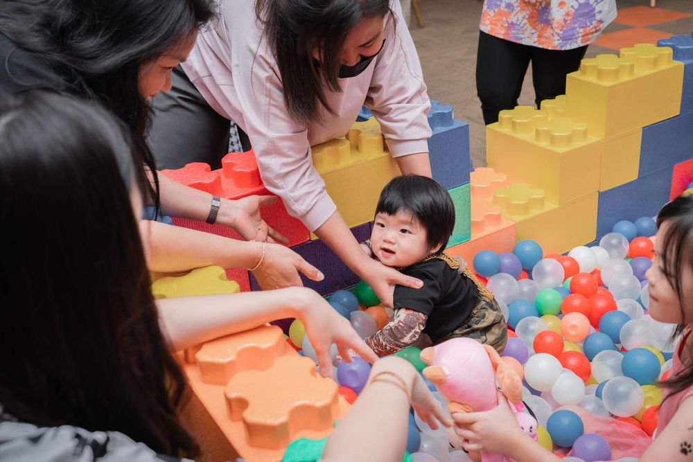 Children playing in a colorful ball pit with large building blocks in the background.