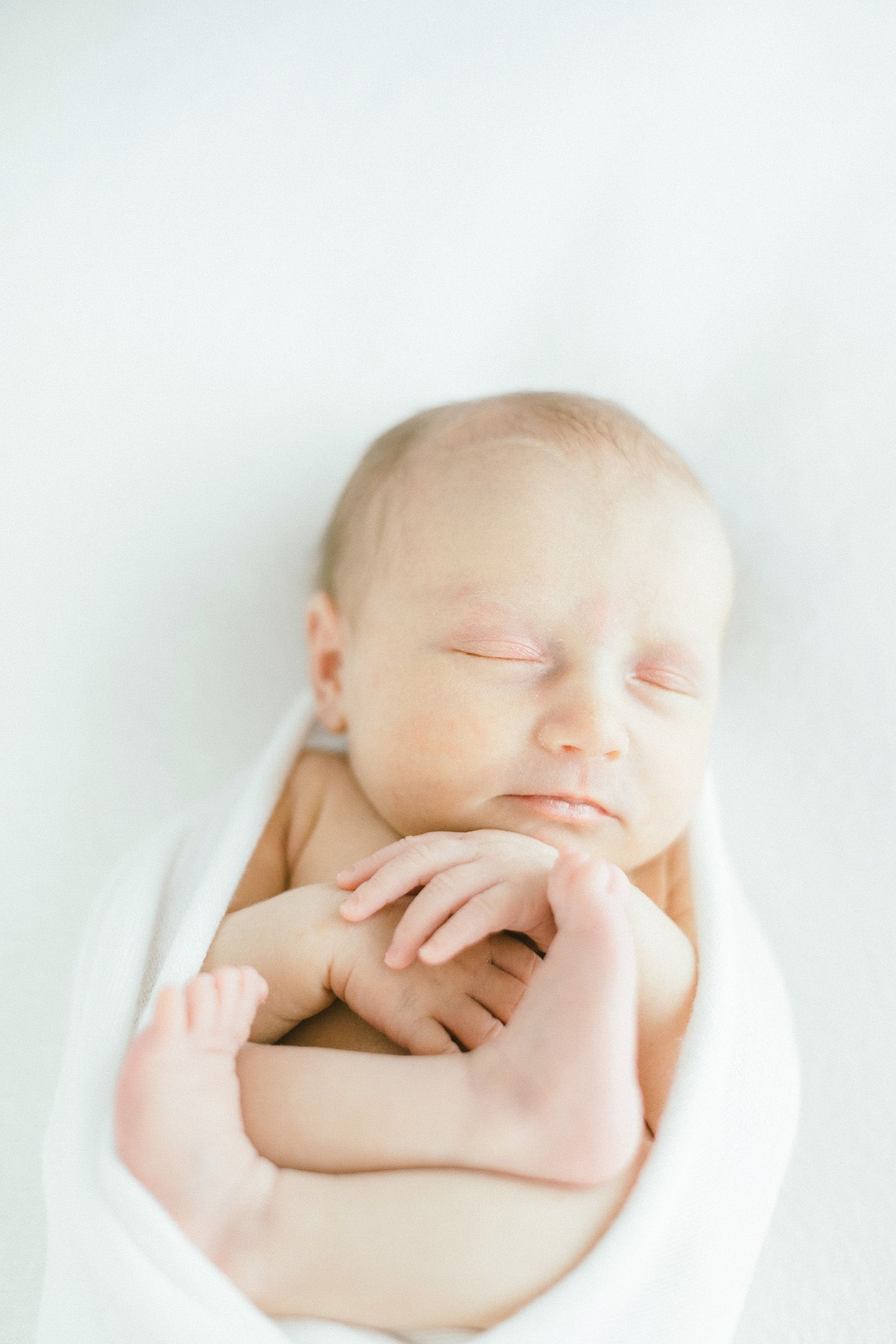 Peaceful newborn portrait with soft lighting and white background.