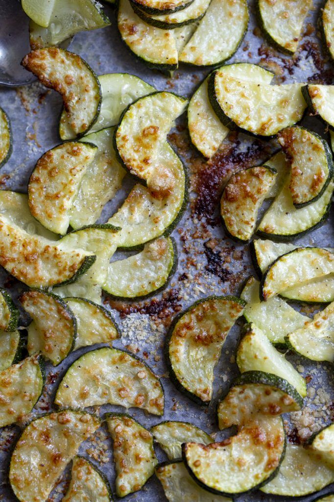 Roasted zucchini slices with herbs and seasoning on a dark baking sheet.