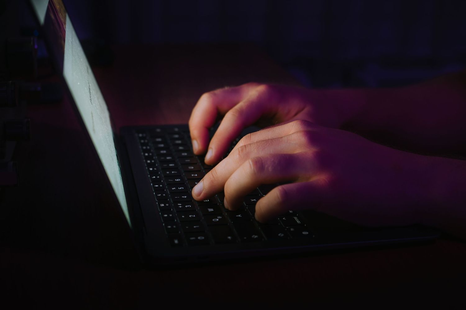Kéz a laptop billentyűzetén sötét háttérrel – modern, letisztult techfotó IT, coworking vagy online munkát bemutató tartalmakhoz.