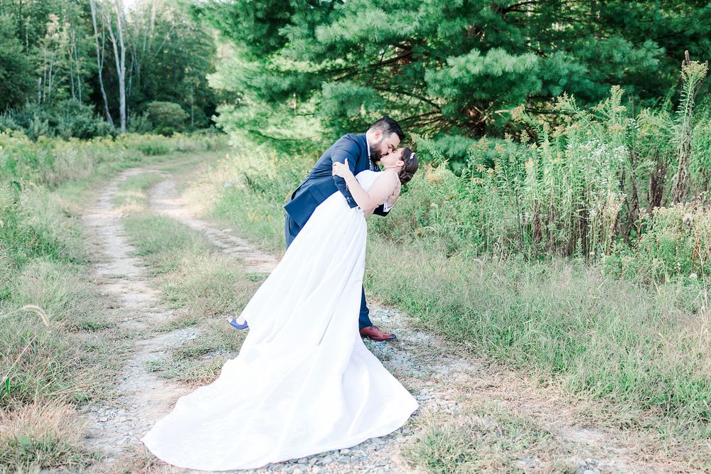 A romantic wedding moment captured on a rustic dirt path surrounded by lush greenery.