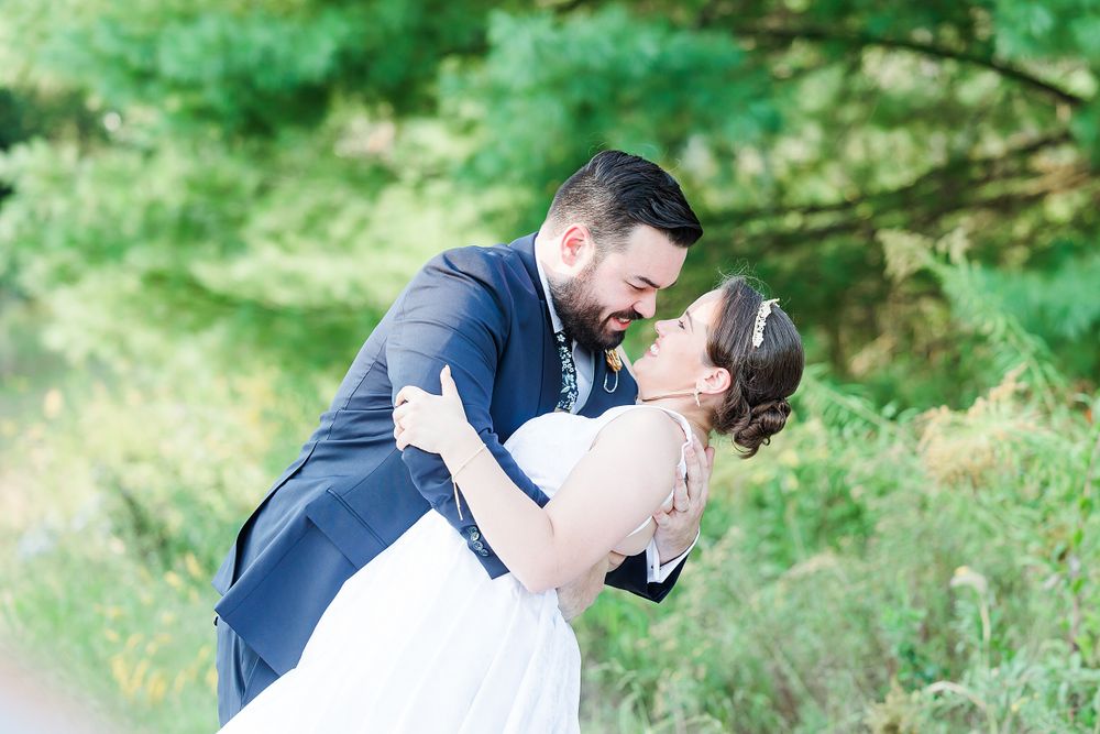 Romantic dip pose between couple in wedding attire surrounded by green summer foliage.