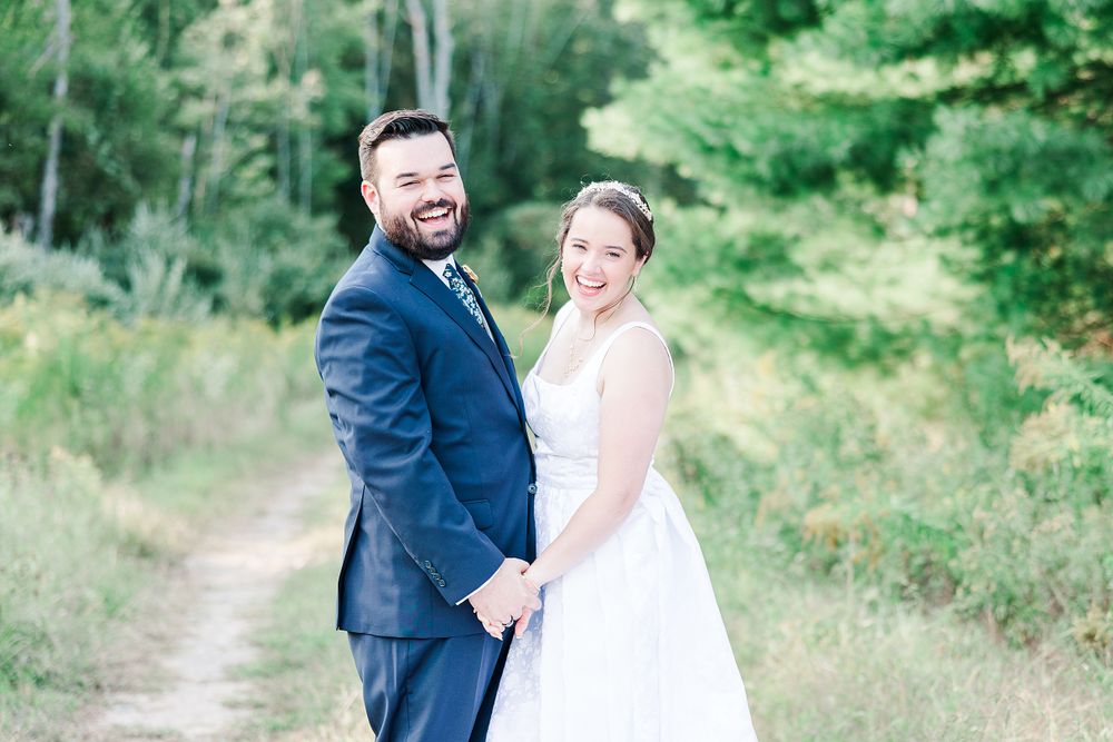 Joyful wedding couple poses on rustic dirt path with long flowing white dress train.