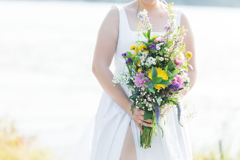Colorful wildflower wedding bouquet with yellow and purple blooms held against white wedding dress.
