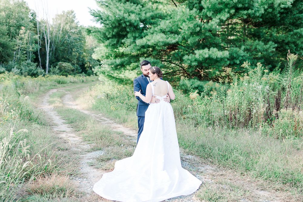 Wedding couple sharing an intimate moment on a winding dirt path surrounded by lush green trees and wildflowers.
