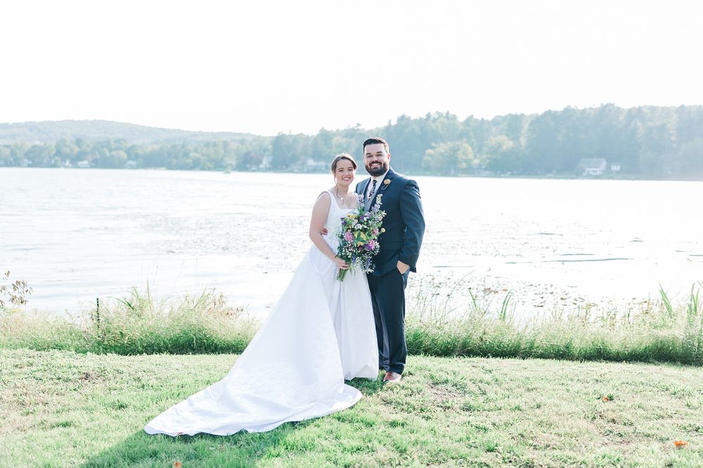 Waterfront wedding portrait with couple standing on lawn overlooking scenic lake view.