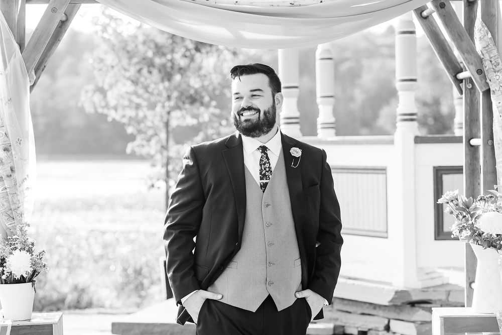 Elegant black and white portrait of groom standing under white gazebo.
