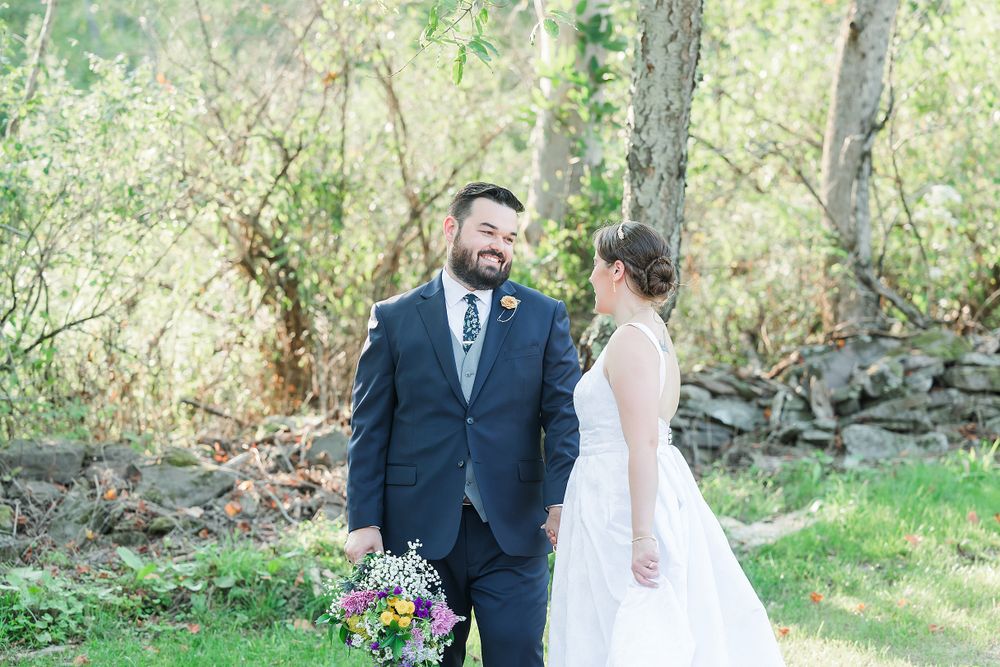 Wedding couple poses in front of natural stone wall and greenery with colorful wildflower bouquet.
