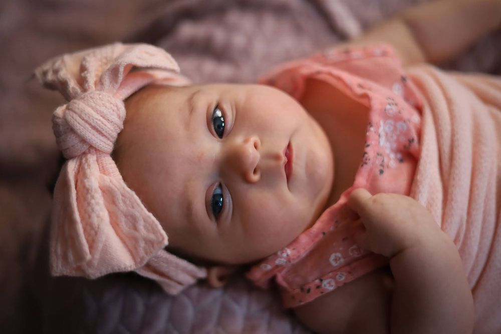 Close up of baby wearing pink bow headband looking at camera.