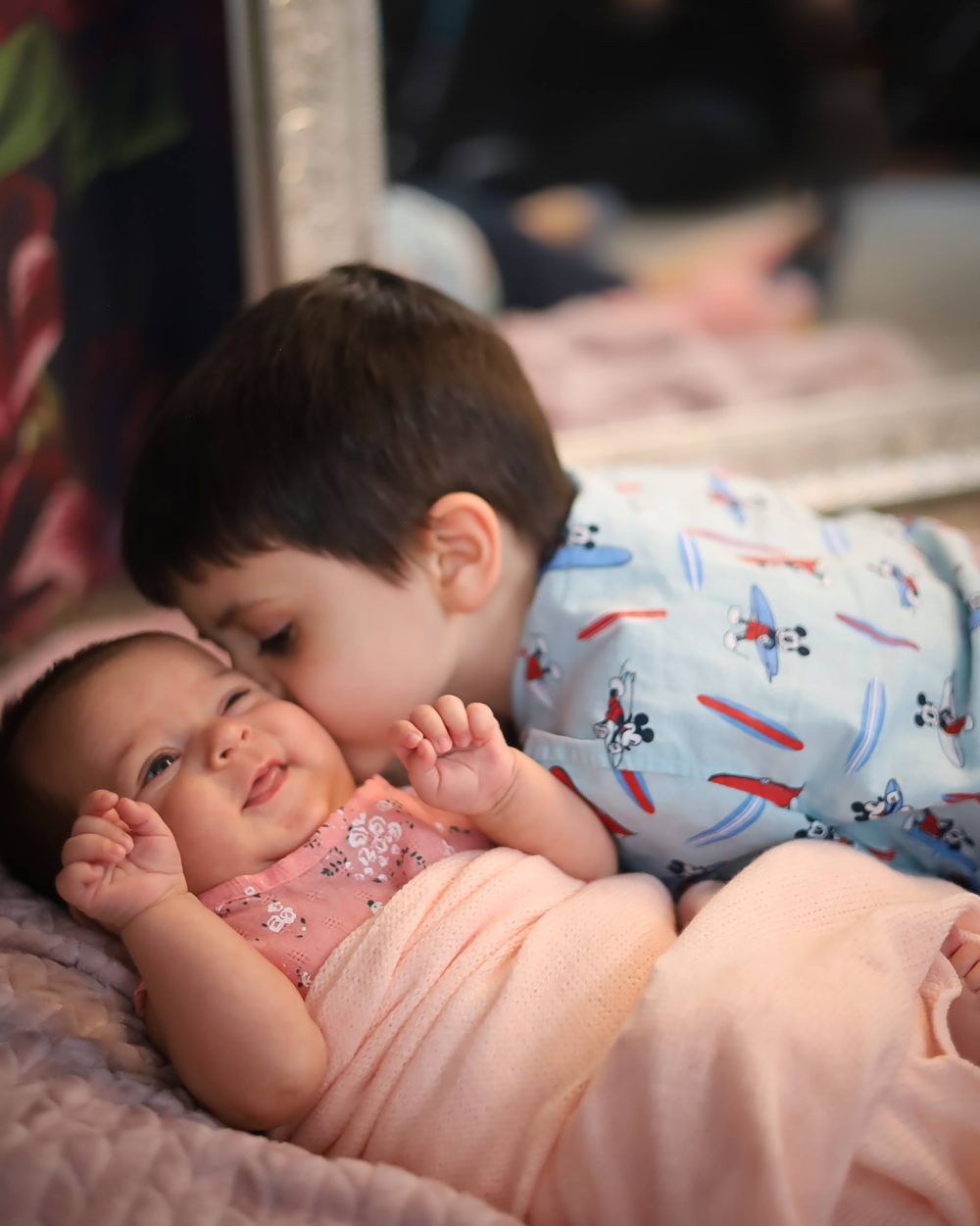 Two children sharing tender moment on pink bedding.