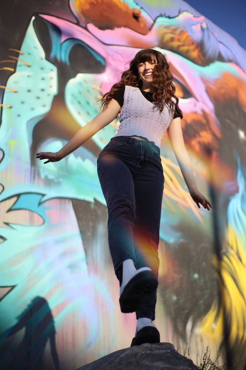 Energetic lifestyle photo against vibrant graffiti wall wearing knit top and denim.