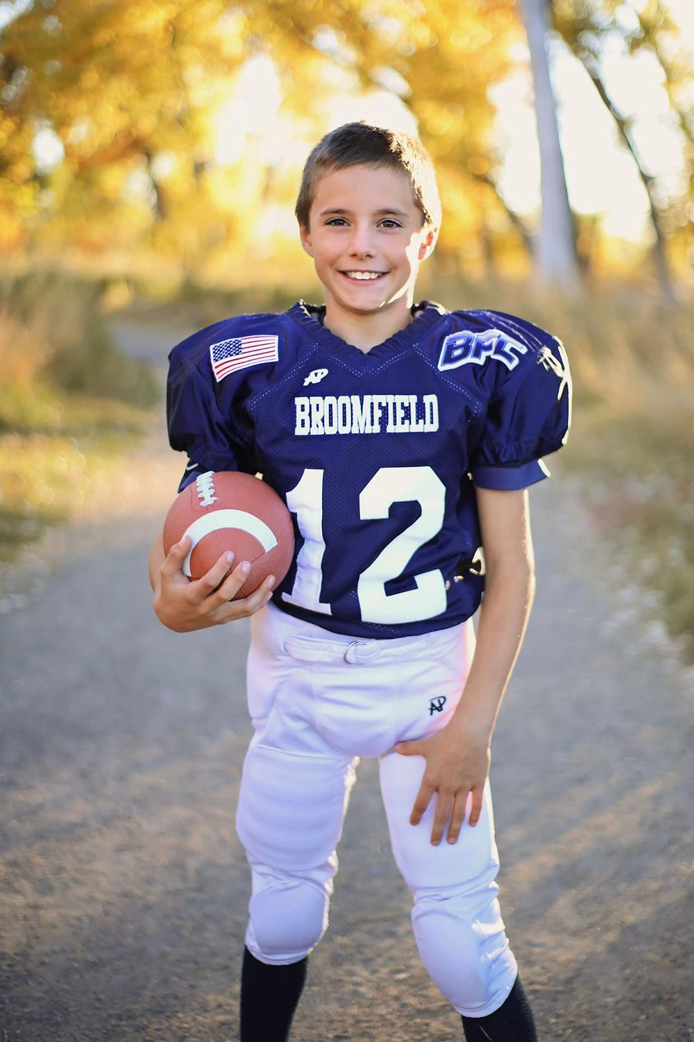Youth football player in Broomfield uniform number 12 poses with ball.