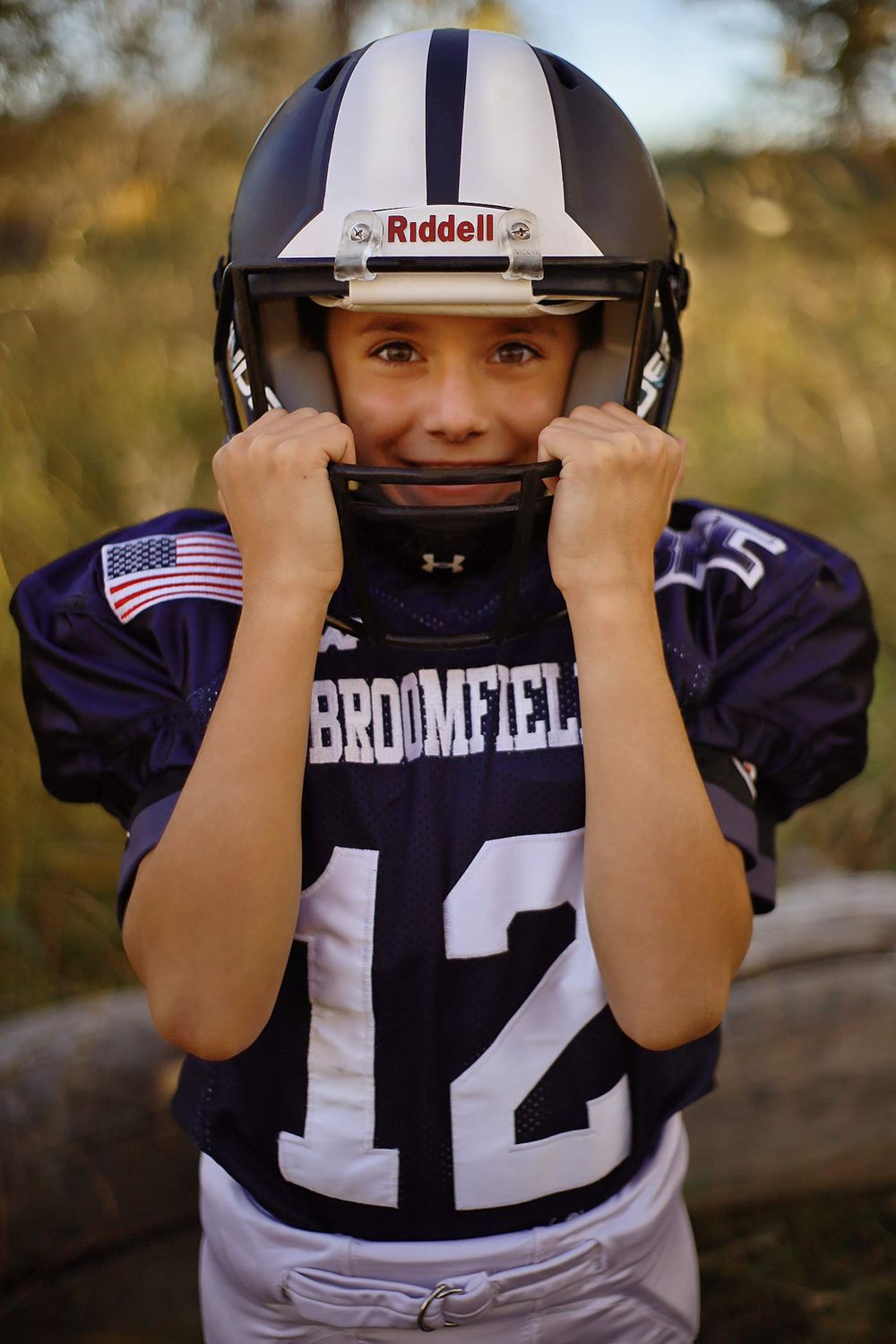 Youth football player adjusting helmet in Broomfield team uniform.