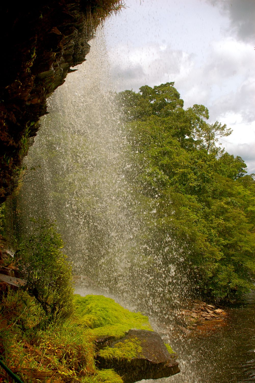Misty waterfall spray creates a ethereal scene against lush green foliage and mossy rocks.