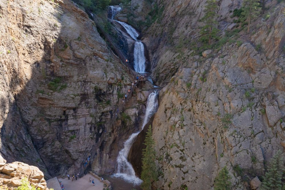 Dramatic waterfall cascades down steep rocky canyon walls in bright daylight.