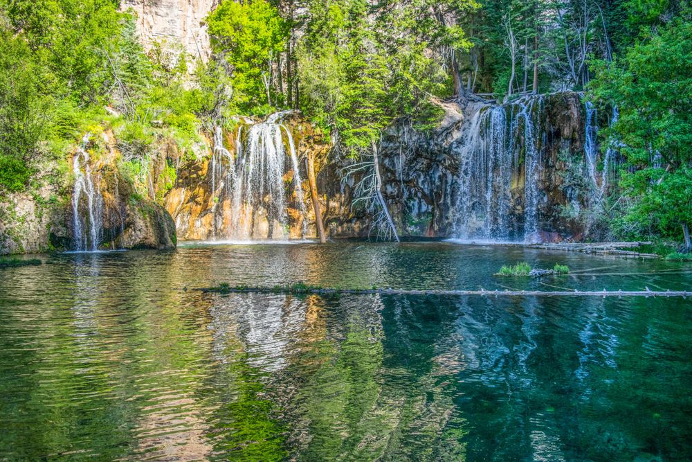 Serene waterfall flows into turquoise pool surrounded by lush greenery and limestone cliffs.