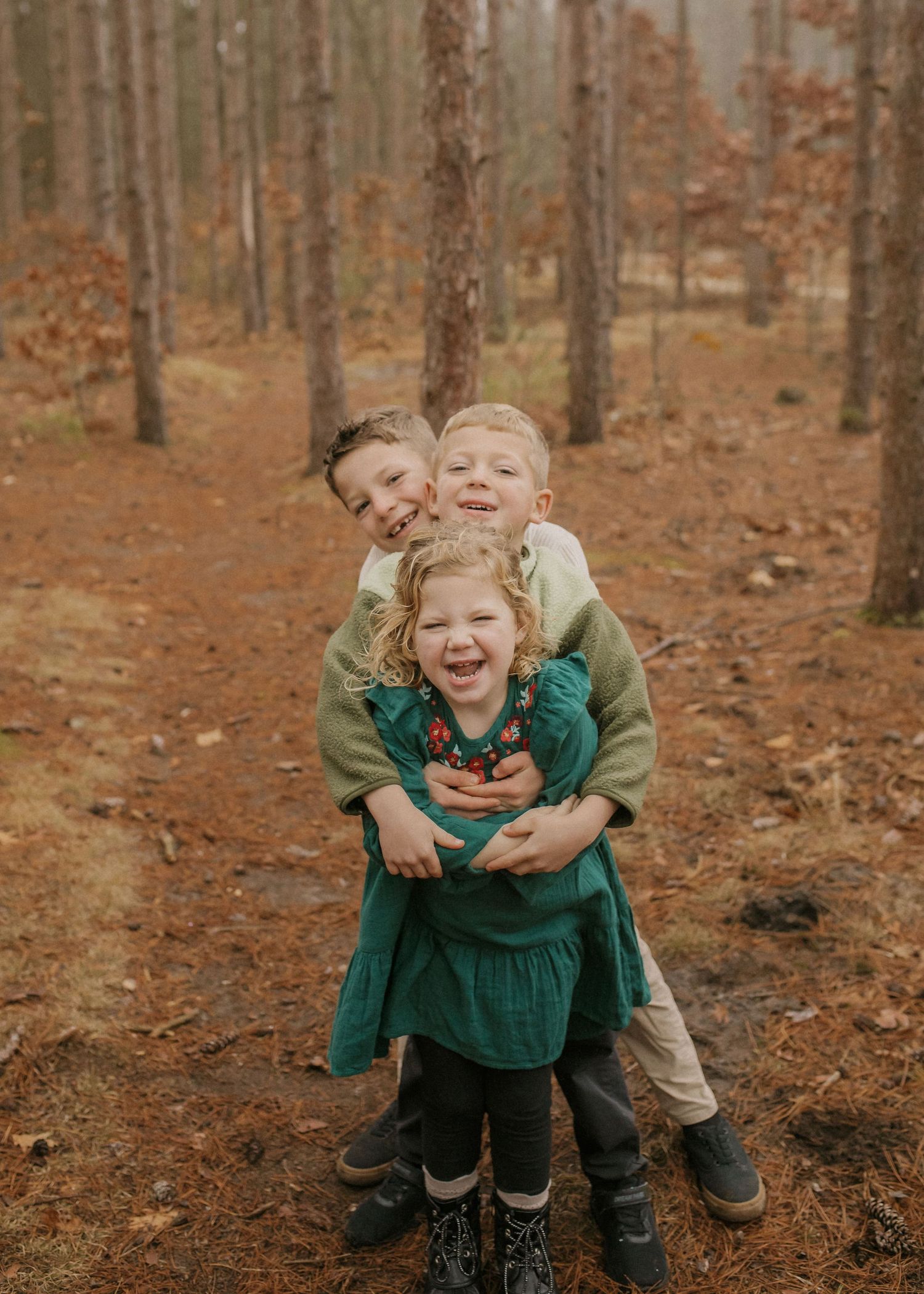 Three children playfully embrace and laugh together among fall foliage in a forest.