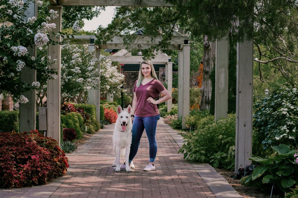 A young woman and her German shepherd are framed amongst pillars and floral overgrowth