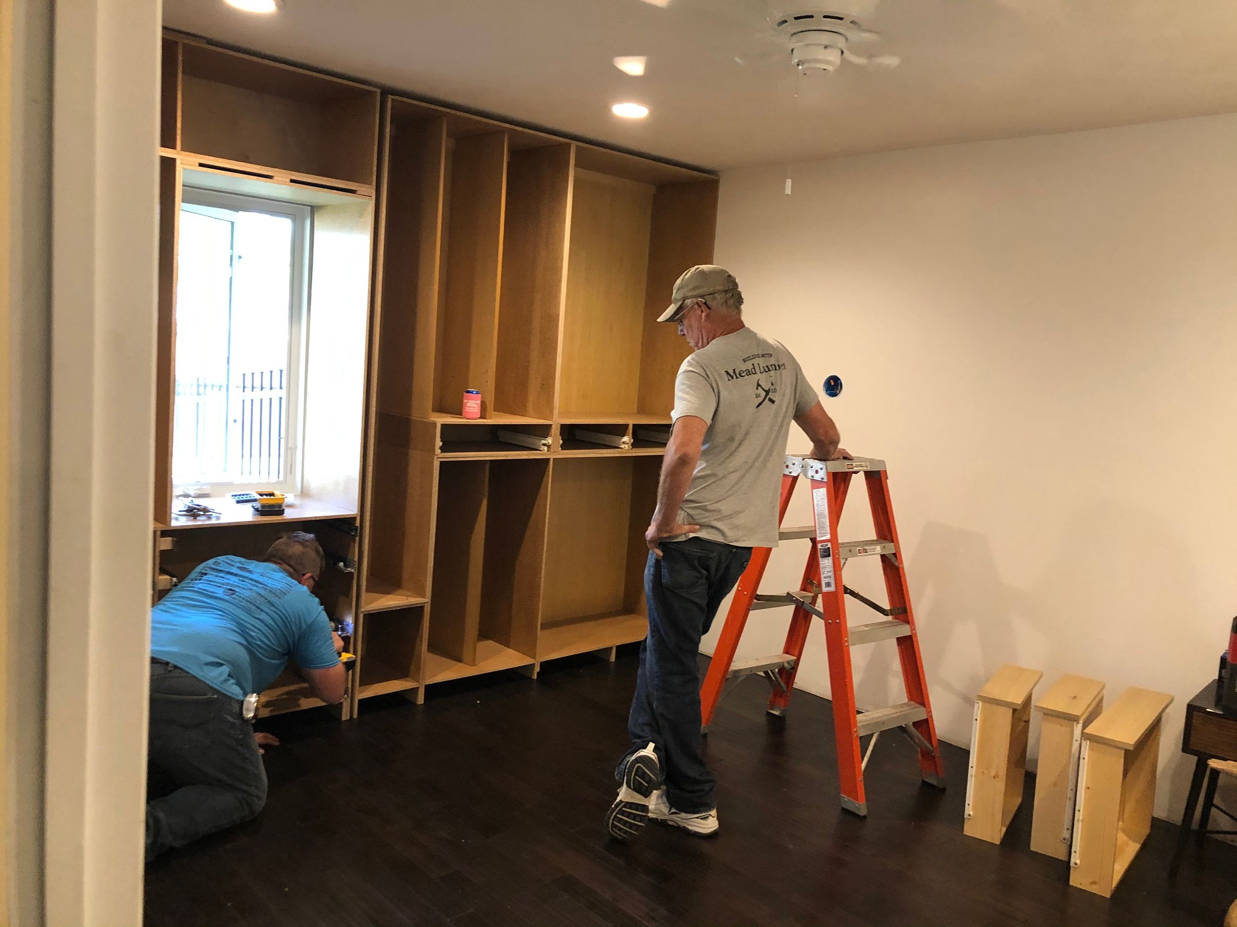 Empty room with wooden storage cabinets and shelving units being installed.
