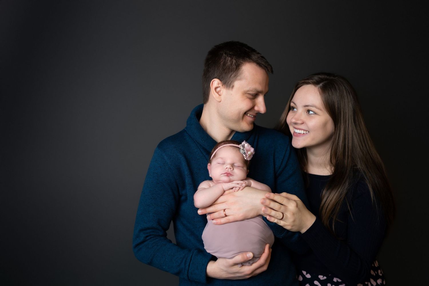 Family portrait session with newborn baby against dark background.