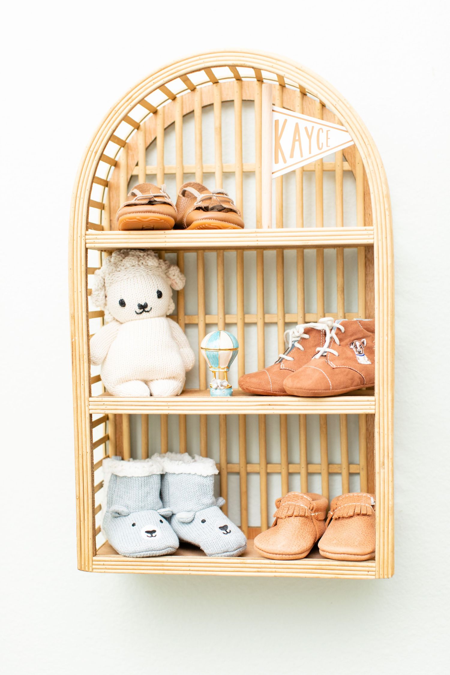 Arched wooden shelf displaying baby shoes, stuffed animals and decor items.