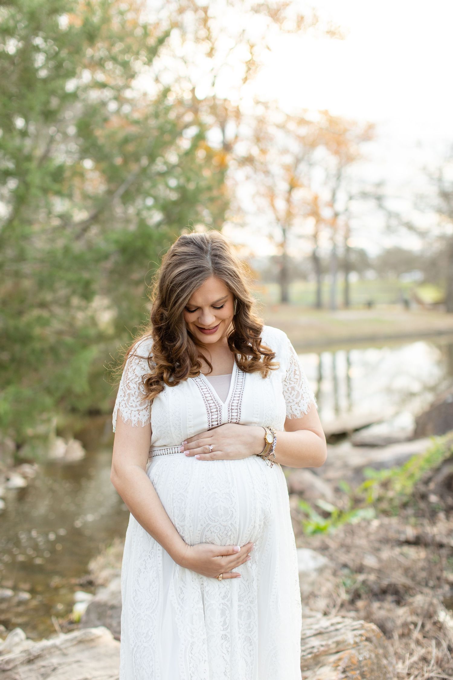 A radiant maternity portrait by a stream with autumn trees in background.