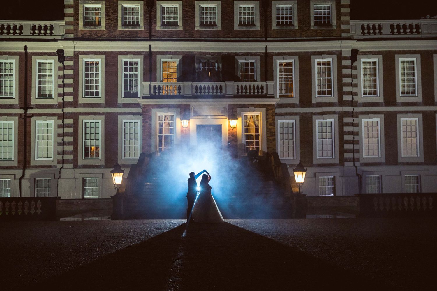 The silhouette of the bride and groom dancing in blue smoke, in front of Knowsley Hall at night