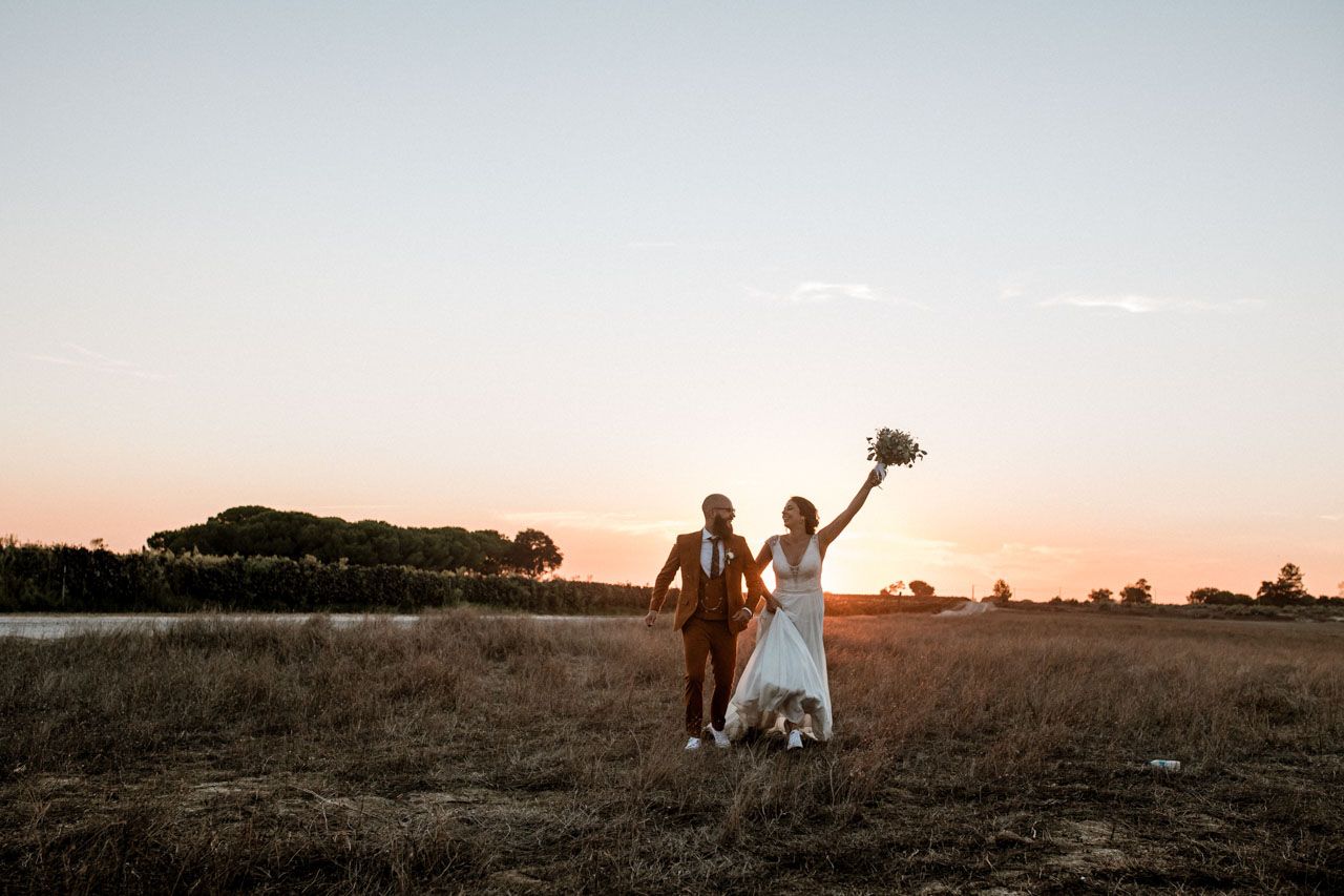 Two figures celebrating in a rustic field at sunset while one holds a bouquet overhead in celebration at Quinta das Riscas