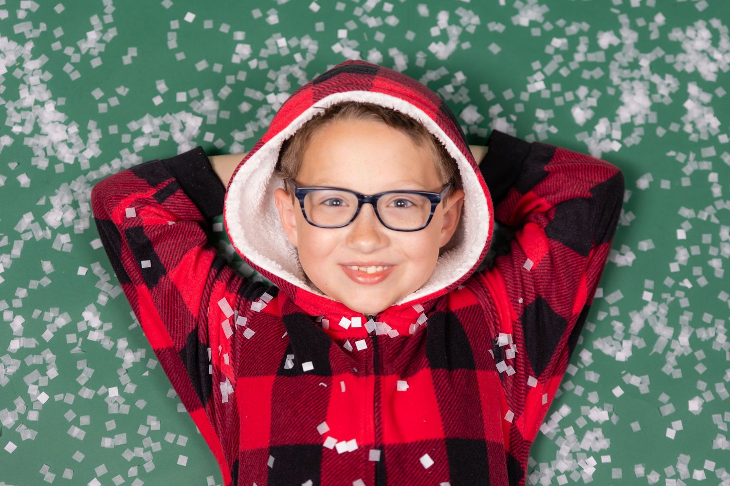 boy child in plaid christmas pajamas laying on green backdrop in studio with fake snow in clayton new jersey Gloucester