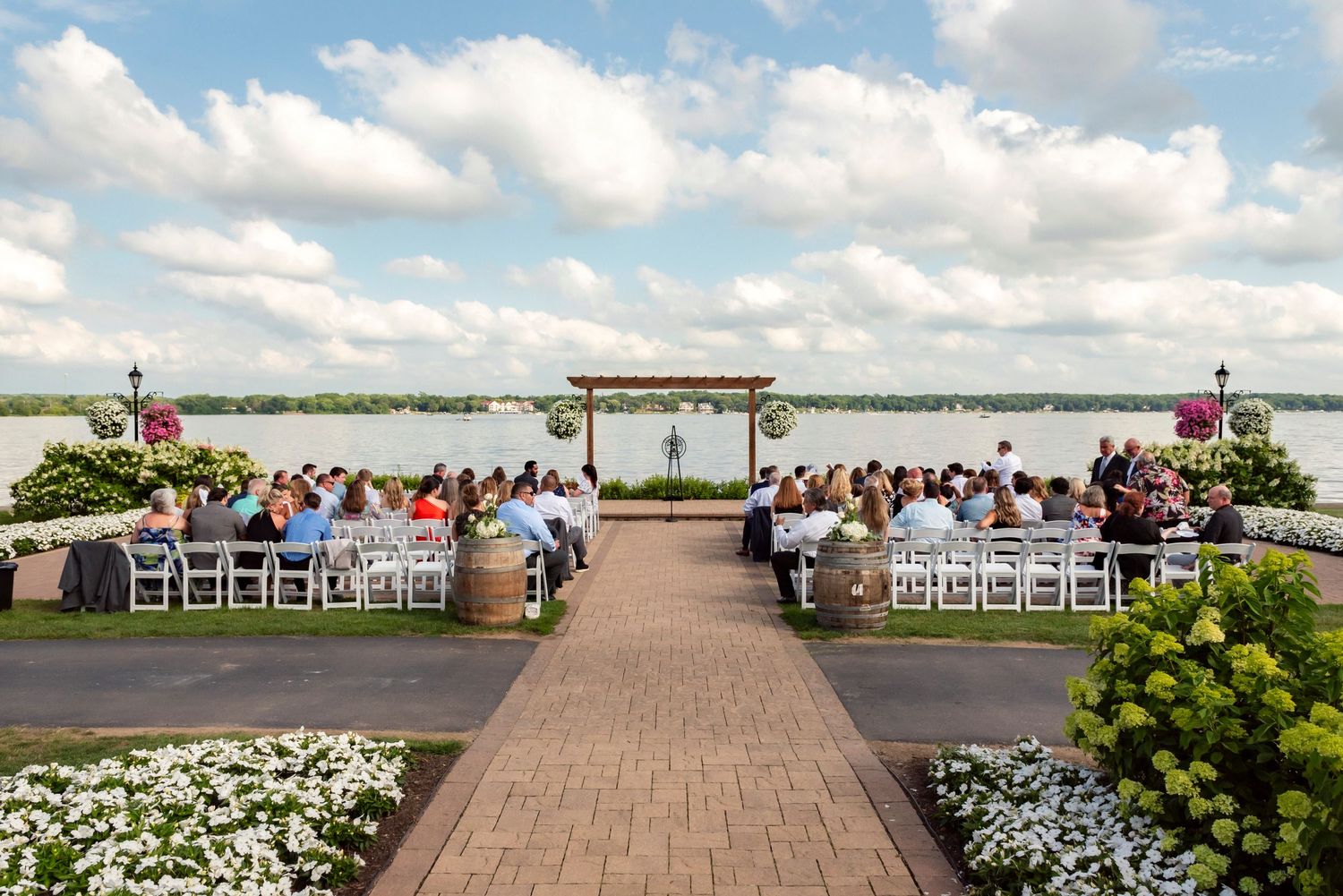 Waterfront wedding ceremony setup with white chairs and floral arrangements overlooking a lake.