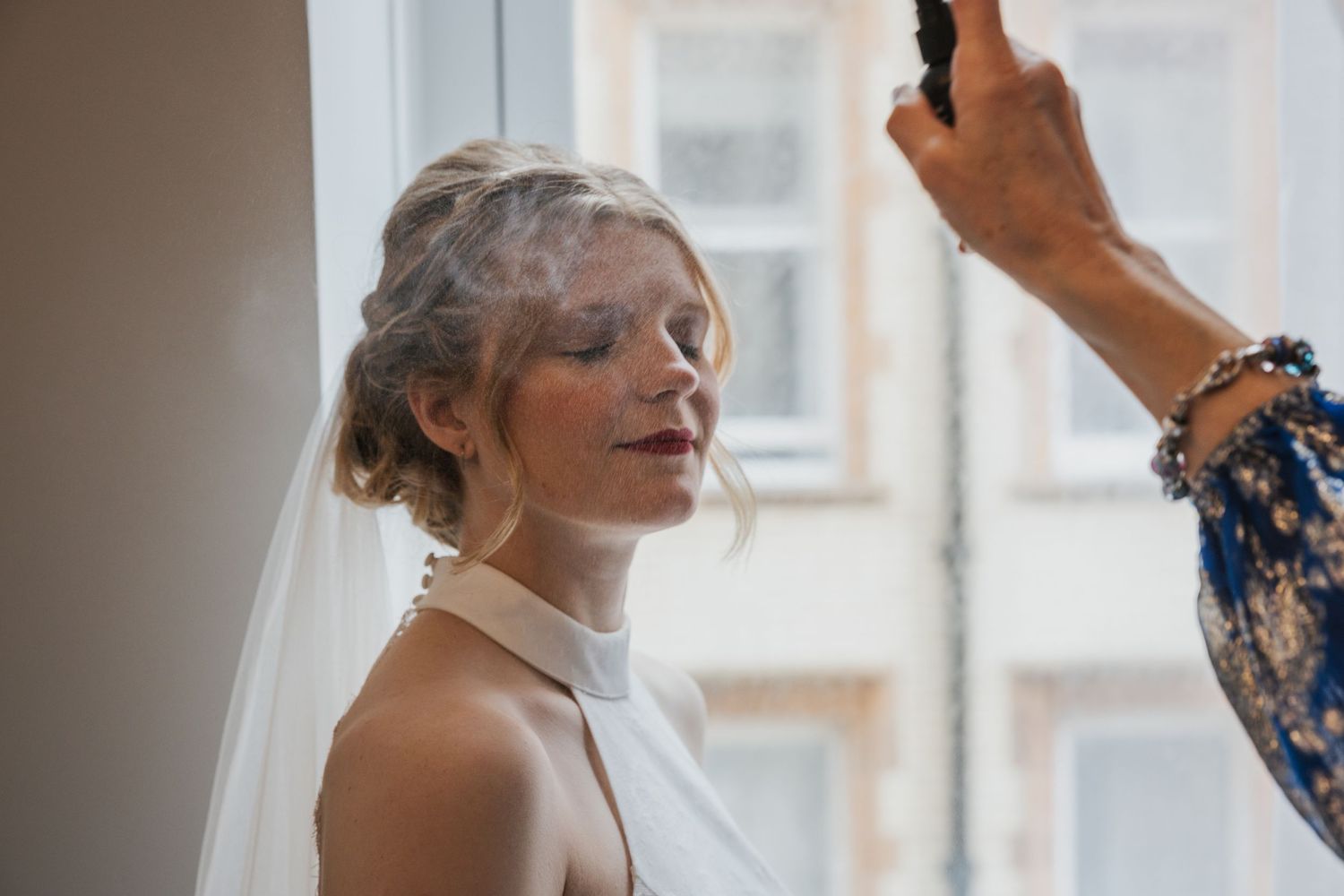 Emma a beautiful blonde bride having her make up set by her mum there is mist in the air